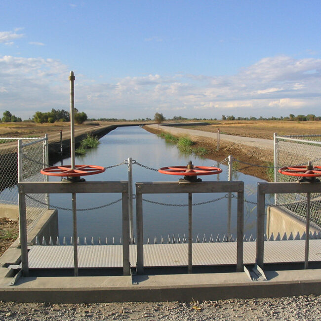 A canal full of water, a cement weir with 3 large red wheels that operate the floodgates.